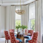 Dining space with red patterned chairs and sculptural gold chandelier.
