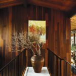 Wood-paneled hallway with large ceramic vase, abstract painting, and black railing in a midcentury home by Sashya Thind.
