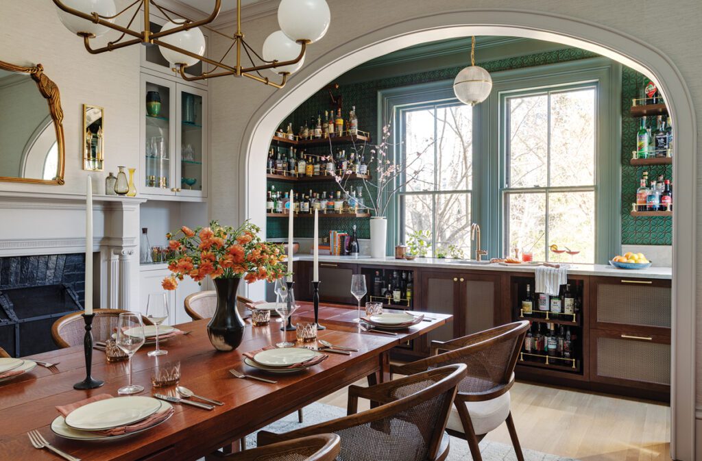 Sophisticated dining room with arched bar opening, green walls, and midcentury lighting.