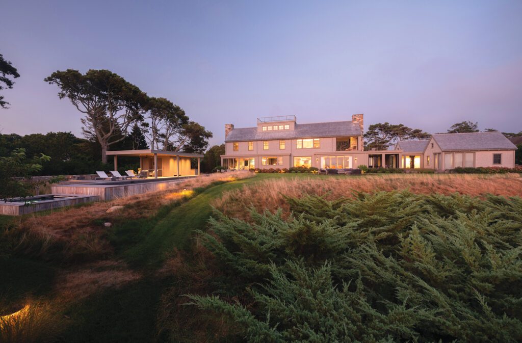 Coastal estate at dusk with illuminated windows and expansive landscaped grounds.
