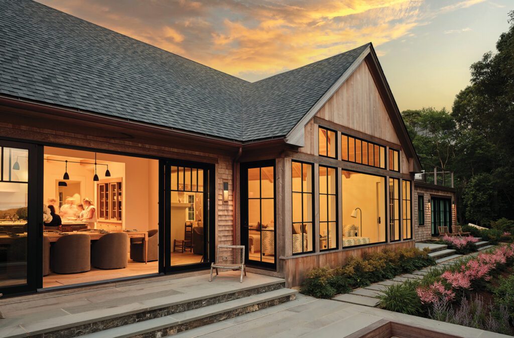 Coastal home exterior at twilight with illuminated glass walls and expansive outdoor terrace.
