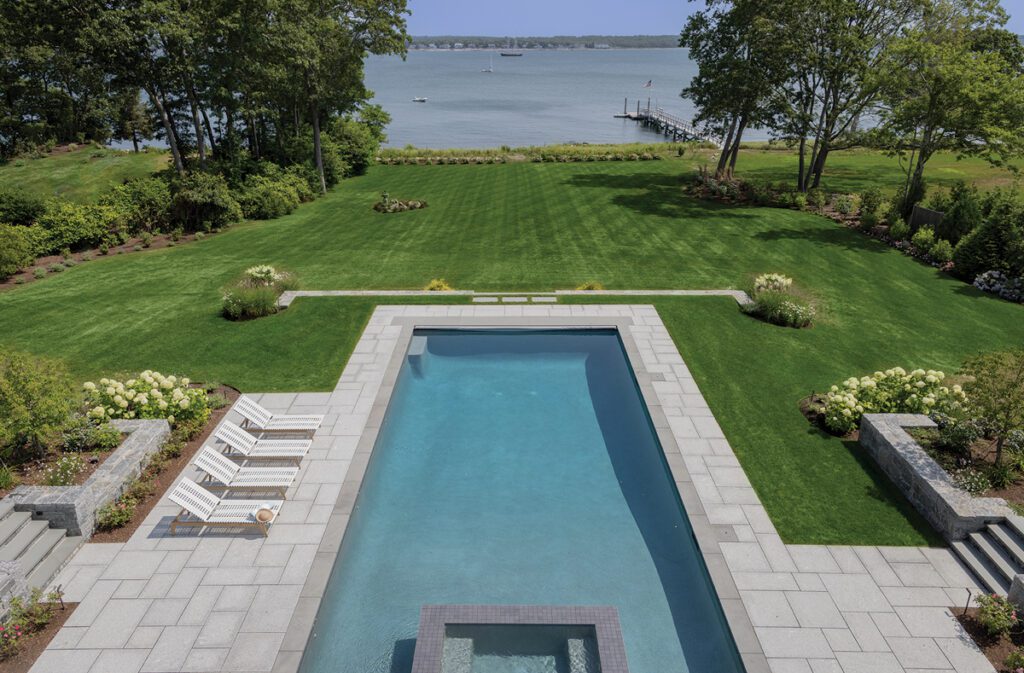 Rectangular swimming pool surrounded by stone terraces, gardens, and mature trees.