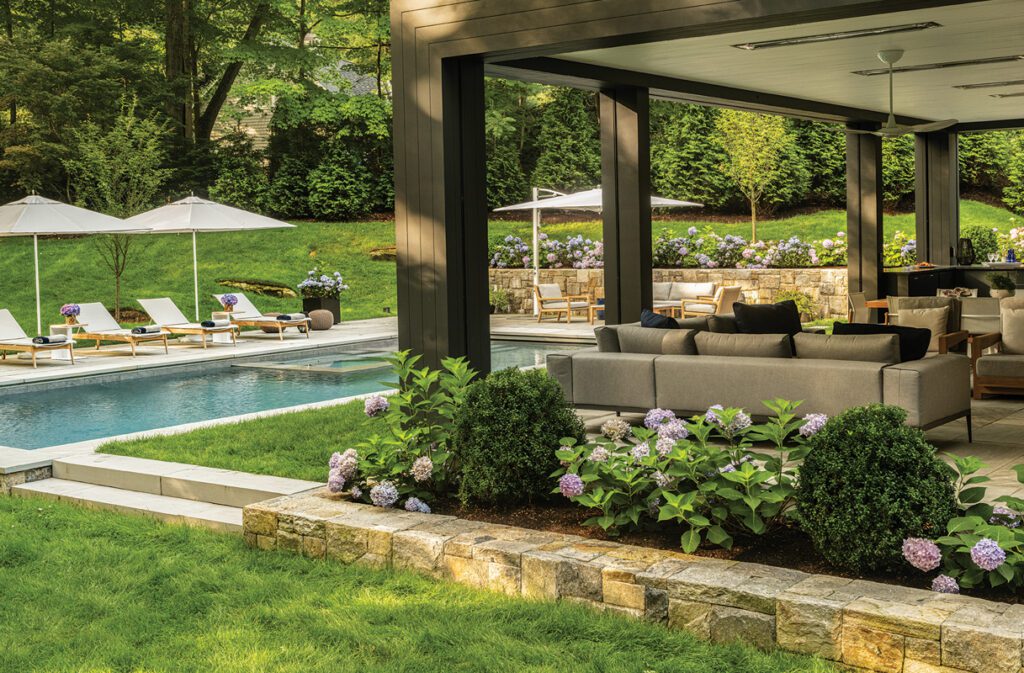 Covered outdoor living pavilion overlooking a swimming pool and landscaped backyard.