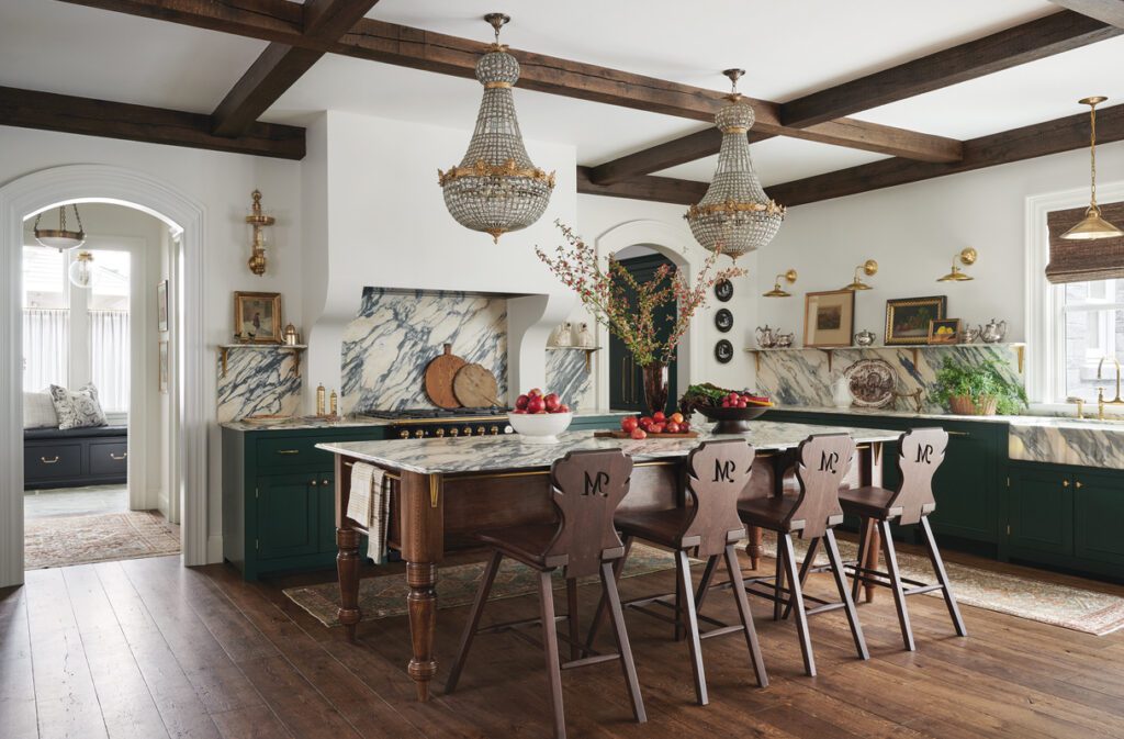 Traditional kitchen with green cabinetry, marble counters, wood island, and crystal chandeliers.