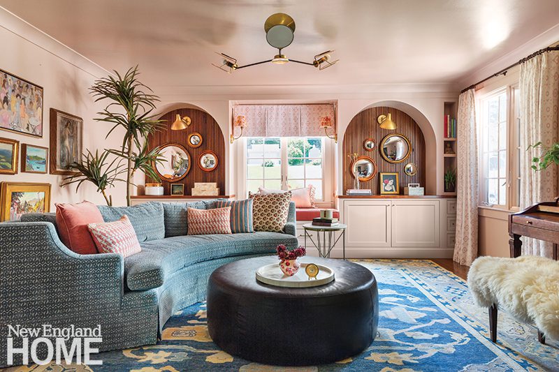 Colorful music room with curved blue sectional sofa, black leather ottoman, patterned rug, and arched wall niches.